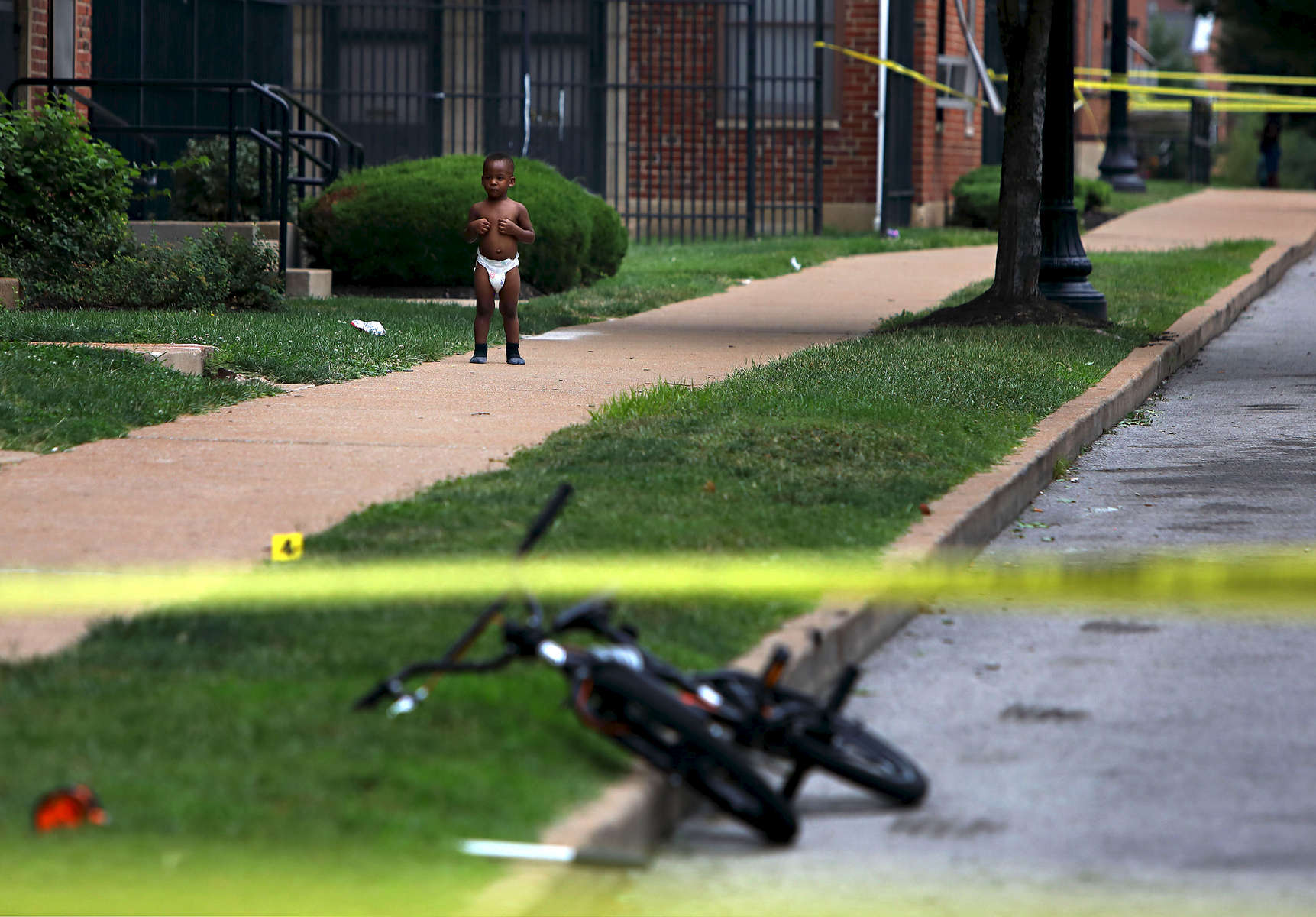 Toddler Donovan Allen, 2, stands outside his home in the 1100 block of Dillion Street as police investigate a fatal shooting in the 1400 block of Kealty Lane in St. Louis on Monday, Aug. 7, 2017. Donovan's mother, not pictured, was sitting on the front steps of her home to the left watching police investigate the scene. Police tape and evidence markers denoting bullet casings were put up right outside the front steps of the Allens home. It was the third fatal shooting in a month that occurred within 100 yards of Donovan's home. The suspect in the shooting returned to the scene driving a minivan and surrendered to police, who recovered a gun from the vehicle.Photo by David Carson, dcarson@post-dispatch.com