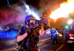 A member of the St. Louis County Police tactical team fires rounds of tear gas into a crowd of people in response to a series of gunshots fired at the police during demonstrations along W. Florissant Road near the QuikTrip in Ferguson, Mo. on Monday, Aug. 18, 2014.  Protesters also threw bottles and rocks with at least one rock striking an officer in the arm.