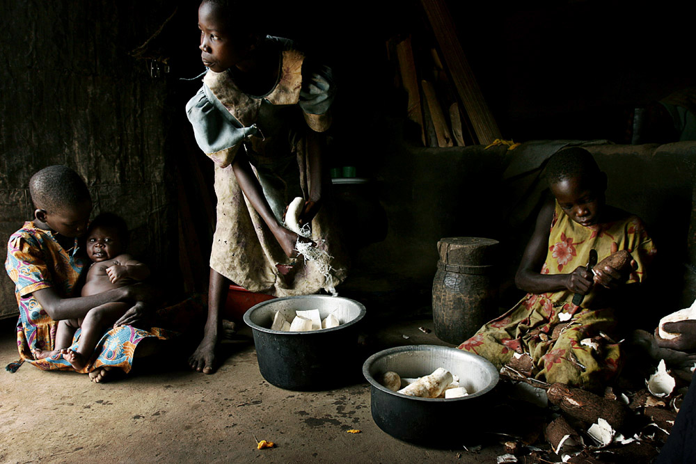 Susan Labol (r), age 10, peels cassava as she prepares a meal with her sister Gladys (c), age 12, for the family on in Laliya, a rural village in Northern Uganda, 2005. Susan is a night commuter, one of about 20,000 children that sleep in nearby Gulu town, as they are afraid of being abducted by the Lord’s Resistance Army (LRA). The rebel group has brought terror to Northern Uganda for almost twenty years, fighting the Ugandan government. The victims are usually children, which are abducted and used as child soldiers and sex slaves. Susan walks 1,5 hour from her home village with her sister Gladys every day to sleep at Noah’s Arch, an NGO housing children in Gulu. They are too afraid to sleep in the village as an older sister was earlier abducted. They walk a further 30 minutes every day to attend school in a nearby village.