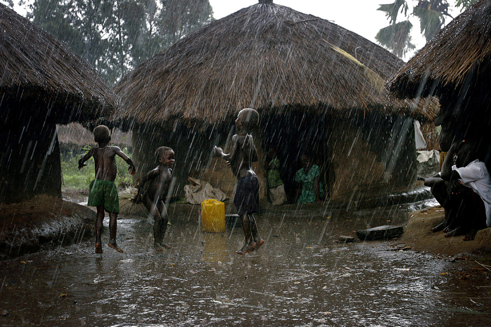 Children play outside huts in a heavy rainfall in Laliya, a poor rural village in northern Uganda, 2005. Many children in this area are afraid of being abducted by the Lord’s Resistance Army (LRA). The rebel group has brought terror to Northern Uganda for almost twenty years, fighting the Ugandan government. The victims are usually children, which are abducted and used as child soldiers and sex slaves. 