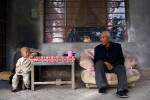 An elderly man sits outside his house with his grandson in a small farming village outside DunHuang, China, 2007