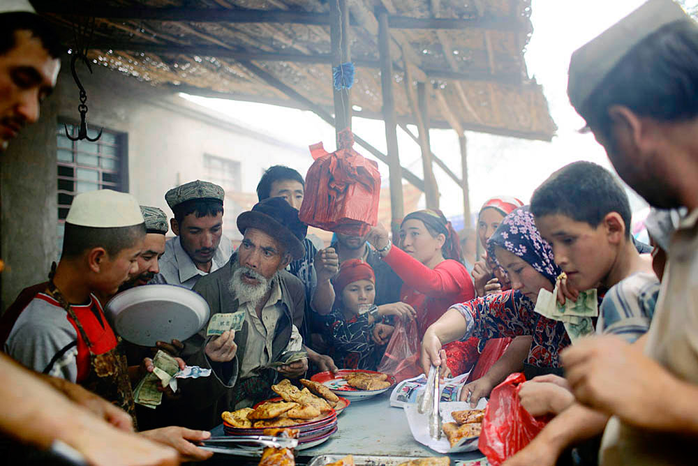 Ethnic Uygur villagers buy food from a stall at a weekly market, Khotan, China, 2007. Thousands of villagers attend every week dressed in traditional clothing. 