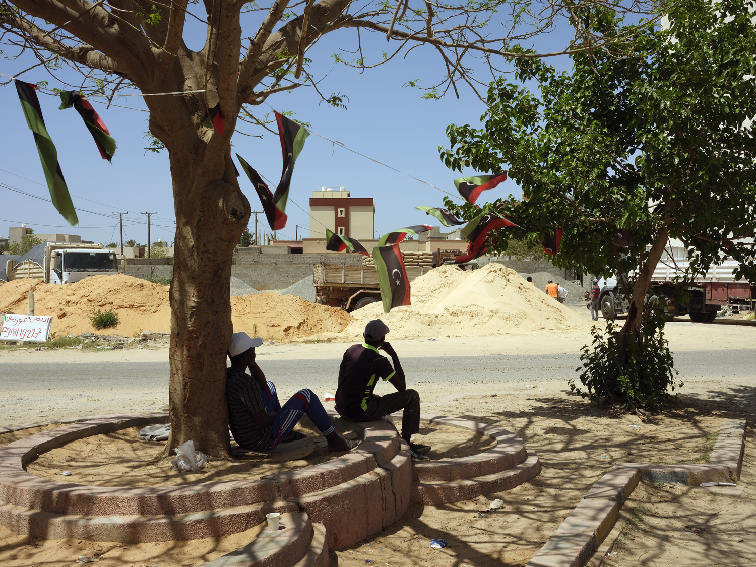 Tripoli, Libya 05/04/2021Across the street from a large construction sight African day laborers take shade under a tree. Jehad Nga
