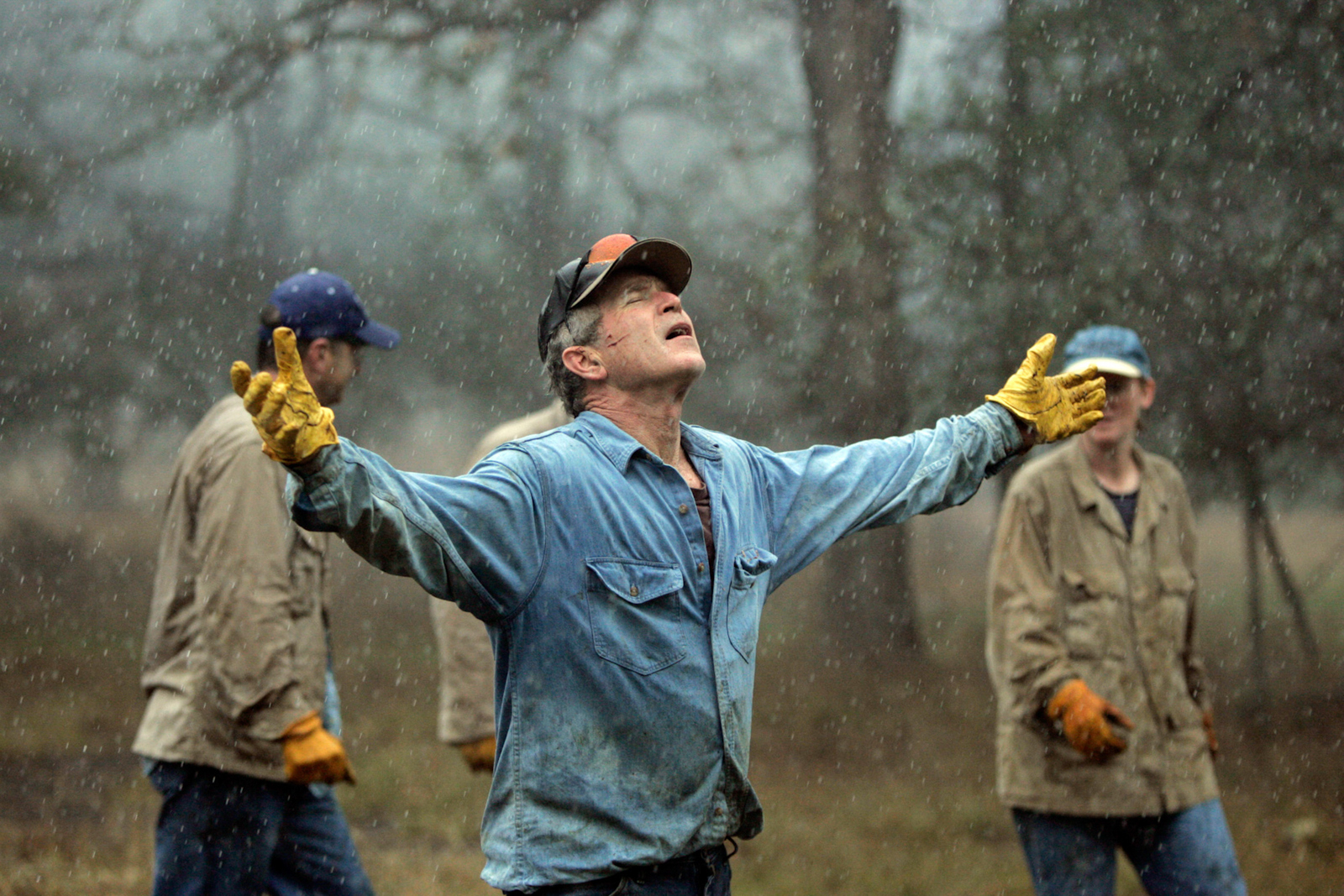 President Bush: Brush clearing and burning with staff. Ranch, Crawford, Texas. The President holds his arms out in the rain.