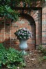 The arched niche is a focal point aloing the backyard crushed path and seperates the home from the neighboring property. This stone urn, filled with seasonal flora, helps soften the brick wall in the backdrop.