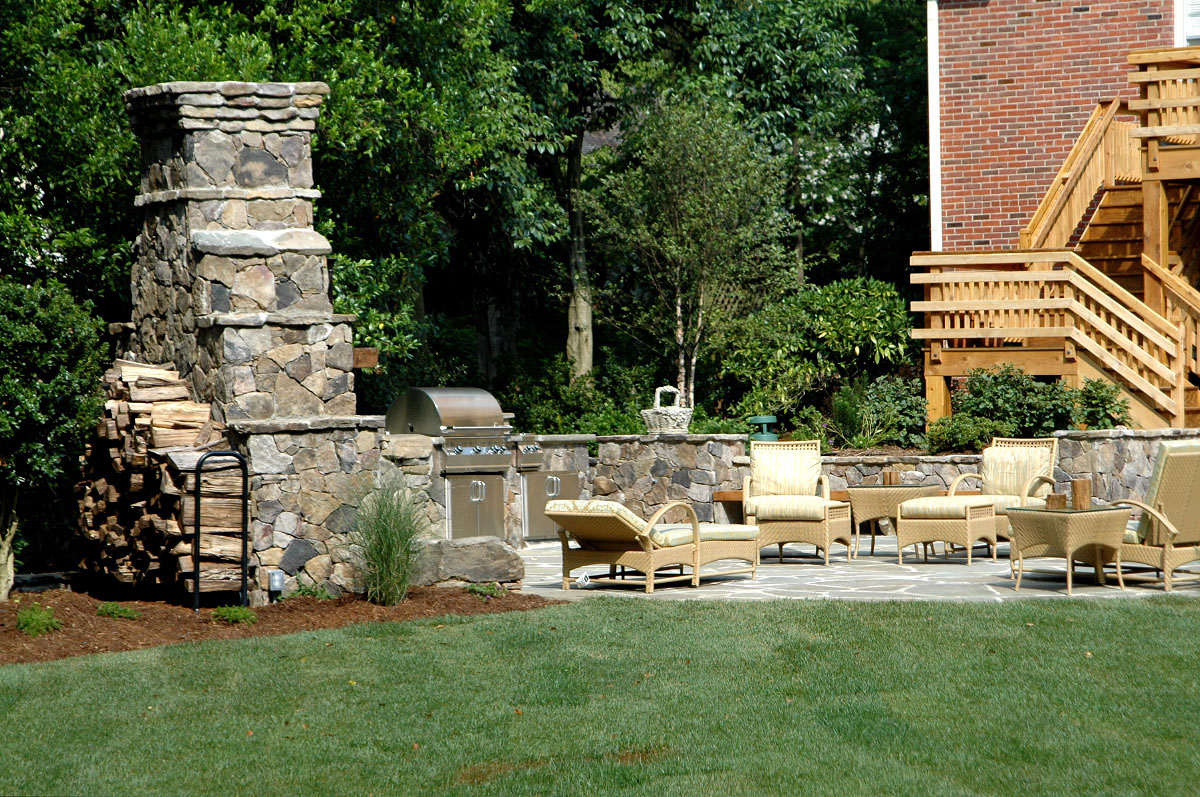 The fireplace wings morph into boulder and stacked stone walls encasing a state-of-the-art grill and stovetop that virtually eliminate multiple trips to the upstairs kitchen. Along with several large boulders and nestled between low stone columns and a raised planter, a 2x8 solid cedar bench supplies additional seating and earthiness to the scene. Similarly, a small semi-circular patio penetrating the main patio consists of oversized field stones with spills of mazus in the joints between. 