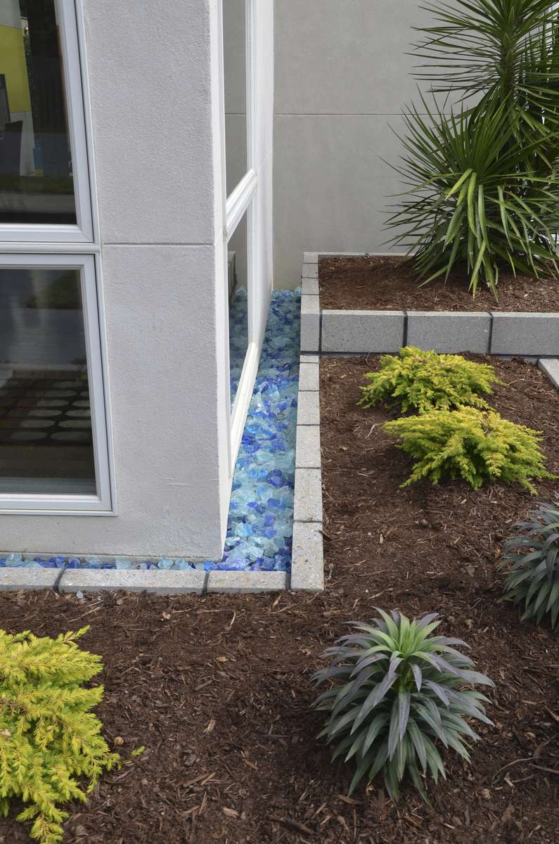 Blue glass block adds interest to the parallel lines of the home's charcoal gray concrete siding. The block sits in a bed built from the same aggregate block used throughout the design...