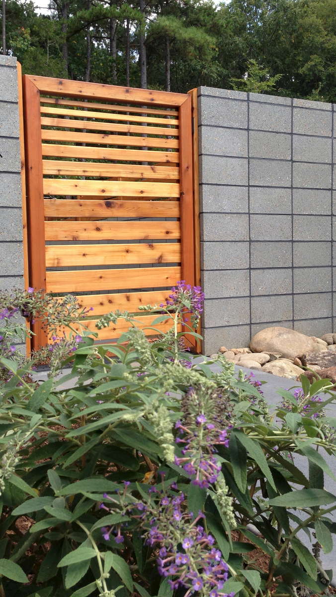 A purple butterfly bush in bloom adds a whimsical point of interest against the contemporary feel of the wall and fencing.