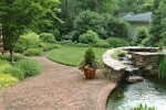 The bricked area adjacent to the water pond serves a dual purpose, as the seperation and connector to the driveway and garage as well as the lead into this lavish backyard.The custom water feature is designed to not only pool on top, but it also features a semi-circular spillway allowing the water to gently flow from the stones before entering the main pool below. 