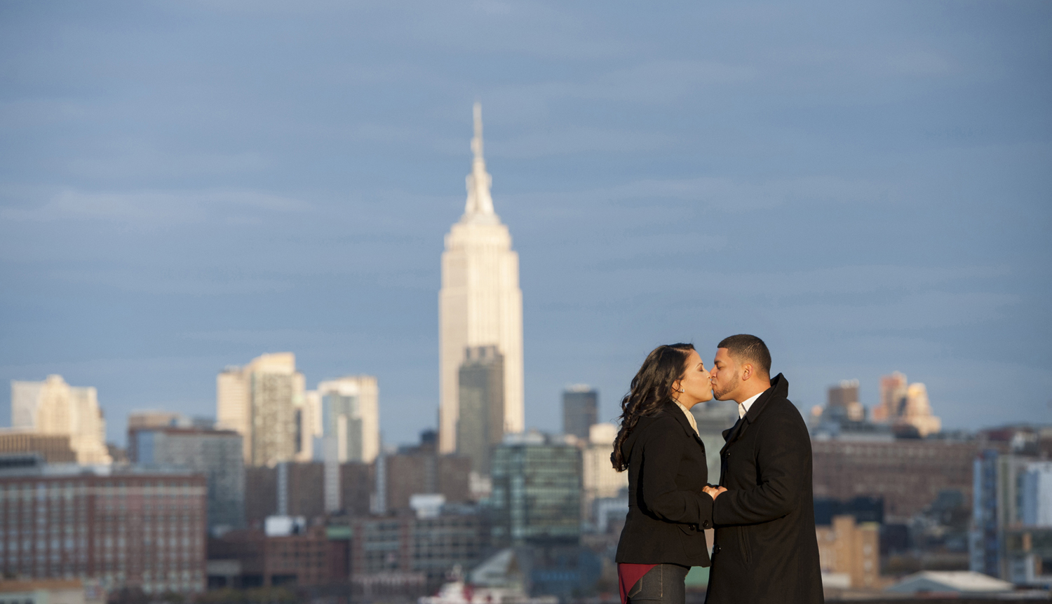 Couple kissing during engagement session in Hoboken with NYC skyline behind them. Hoboken wedding photographers
