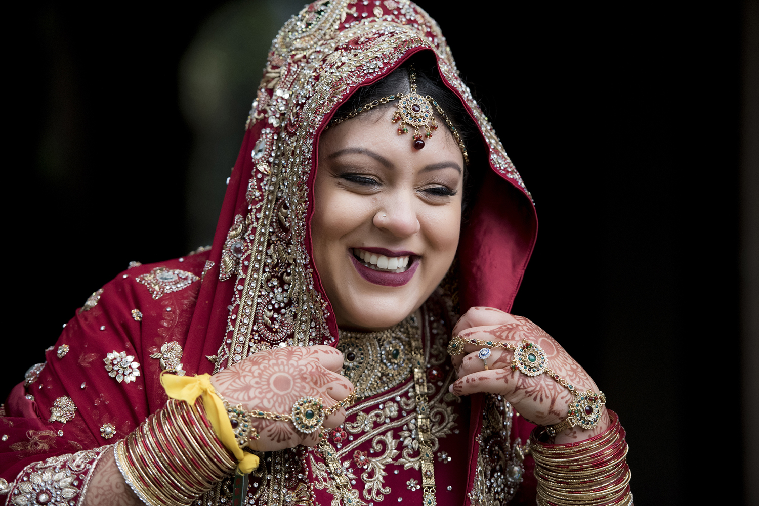 Hindu bride laughing as she adjusts her red and gold outfit
