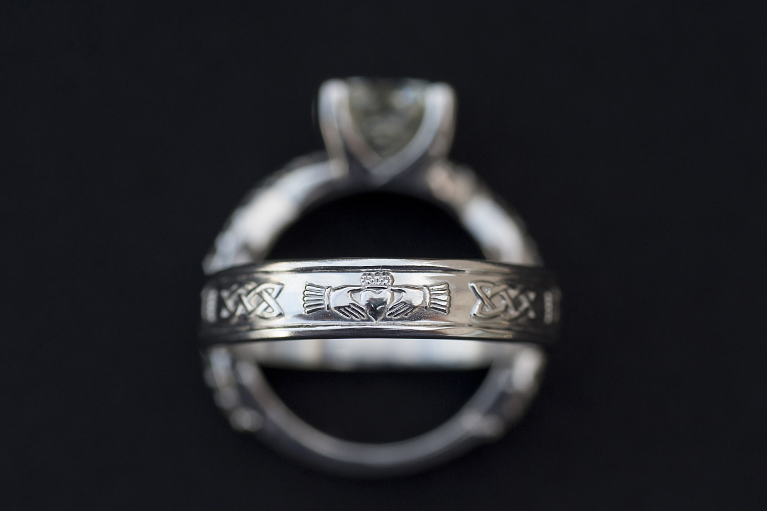 claddagh ring detail with engagement ring against black background. 