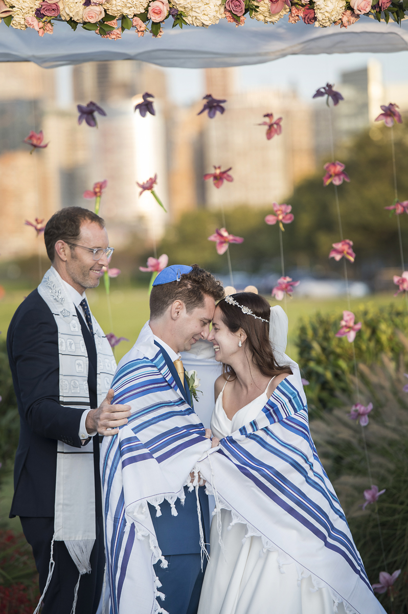 couple is wrapped in a tallis during their Jewish wedding at Liberty House in Jersey City. Jersey City wedding photographer