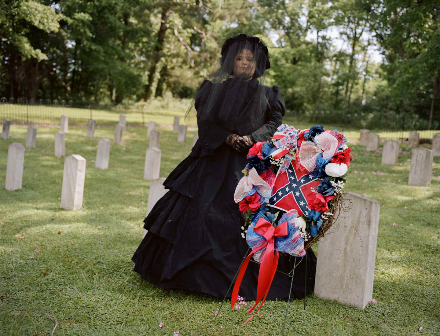 Tara Bradley poses for a portrait in her official “mourning gear”. She is a member of a group called the Order of the Confederate Rose. Though similar to groups like Daughters of the Confederacy, members of this group insist that they are not political and are open to all people. . On April 21, the group laid wreathes at a Confederate cemetery in Raymond, Mississippi for Confederate Memorial Month. The keynote speaker from the local Sons of Confederate Veterans group mentioned Hitler, the KKK and David Duke in his speech. One member of the Roses left in the middle, but it was later discovered that she did not leave in protest but because her feet hurt. After the ceremony, when pushed on dressing up as confederate slaveholders, members repeated false statistics like only 5 percent of Southerners owned slaves (in Mississippi, it was 55 percent), and argued that people also dress up as Union soldiers. When it was pointed out that no one dresses up like slaves, one woman exclaimed, ““We’d love to have someone that would!” All of the women present boasted about volunteer work and civic duty and none thought their costumes or activities were racists or offensive. Groups like the OCR help keep the traditions of the Confederacy – and it’s racists policies – alive and well. 