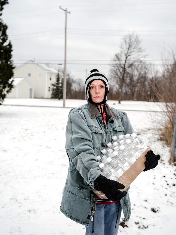 Julie Bennett stops for a photograph after collecting her daily case of water from Firehouse #3, Martin Luther King Avenue, Flint, Michigan, January 27, 2016.