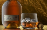 Shot with the camera angle at 0º to the bottle and cropped in a horizontal aspect. The cork bottle stopper is slightly obsured by a lowball glass half filled with ice and Scotch whiskey. The composition is on a pebbly and slightly reflective gold surface and in front of the textural gold back wall. The light is soft and from two directions, the main light is softly from the left side and a top light creates an interesting glow to the gold surface highlighting the whiskey and and adding depth to the subject's reflections in this still life.