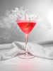 The camera is dead on (zeroed out) to this portrait aspect composition. Vaporization from the liquid nitrogen creates dancing white plumes as the lime wedge drops into this drink splashing the beautifully saturated red fluid made with lime juice, Cointreau, vodka and cranberry juice. Served in a traditional frozen martini glass sitting on an all white reflective bar top with gorgeous light from the right. A fine white linen napkin cradles the back of the glass stem.