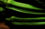 Extreme close up of just picked okra on a wood background. The camera angle is at 45º and the image is cropped in a landscape orientation. The late day light accentuates the highly saturated green of the okra in a very dramatic fashion.