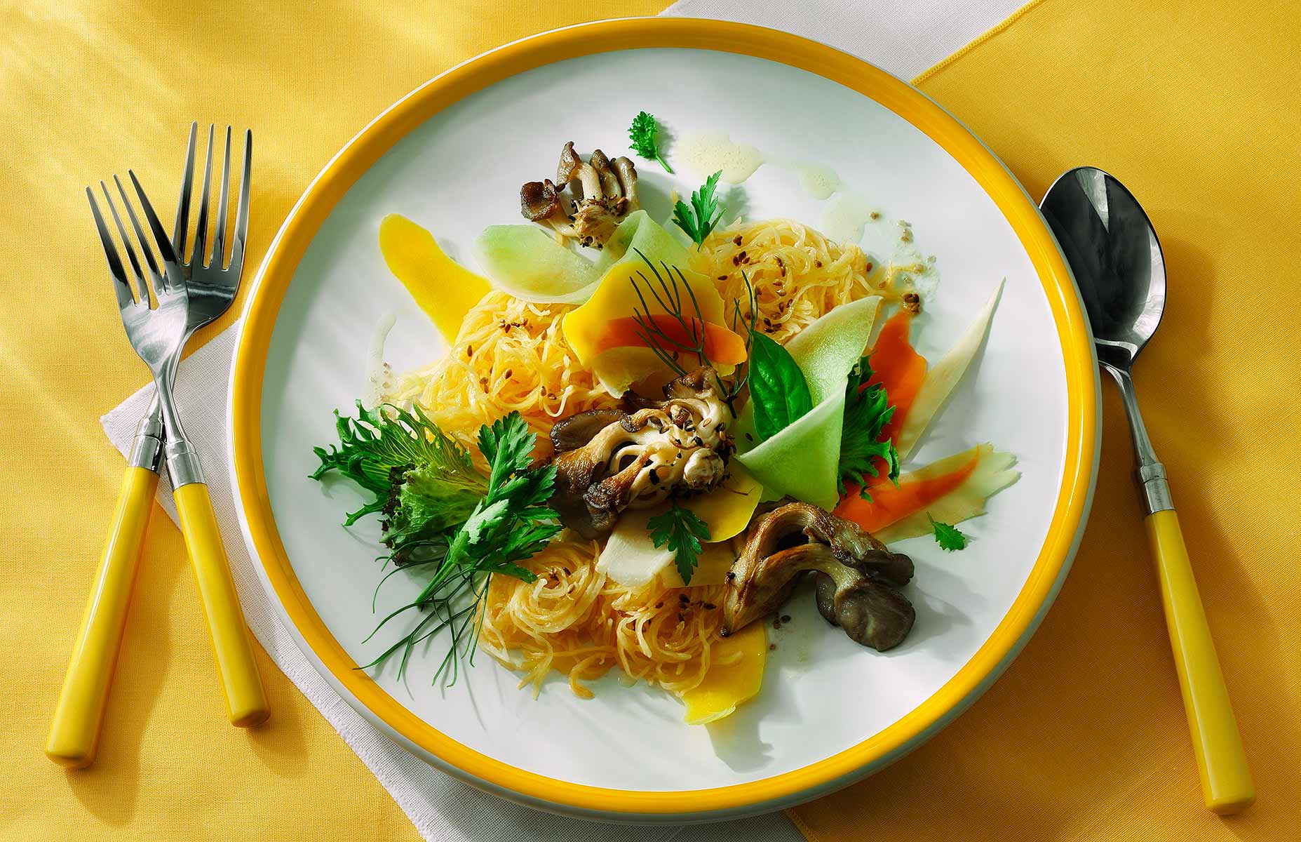 A colorful and bold landscape image evoking the gifts of the new spring season. A slightly overhead angle of view finds the composition on fine bright yellow and white linens. The spaghetti squash is baked and topped with mushrooms, mango slices, honeydo melon, cantalope, carrot shavings and frest herbs. Virgin olive oil is drizzled over all and the streaking light from back left adds intense dimension to the subject.