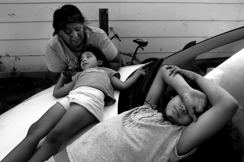 Rachel Ramos, left, talks with her granddaughter Destiny Vargas, 5, center, while her other grandaughter Brooklyn Vargas, 9, right, lays on the hood of their car while taking a break from cleaning their yard of tornado debris in Holly, Colorado. Ramos' house was destroyed by the tornado but they are rebuilding their home. (Photo by Chris Schneider)