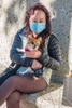 An Asian woman, wearing a face mask holding her dog while resting on a concrete bench in Santa Barbara, California.