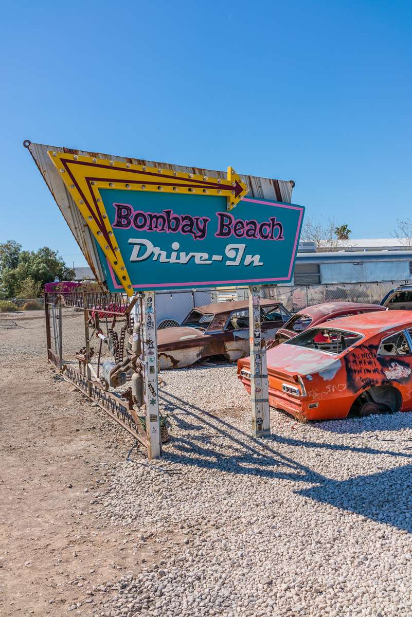 Bombay Beach Drive-In is a fake drive-in cinema that is really a group of junked cars arranged as though they were facing a drive-in movie screen. A trailer from a tractor trailer truck serves as the screen being painted all white.The drive-in's sign is shaped like a Mid-Century sign with its sharp angles and colors.