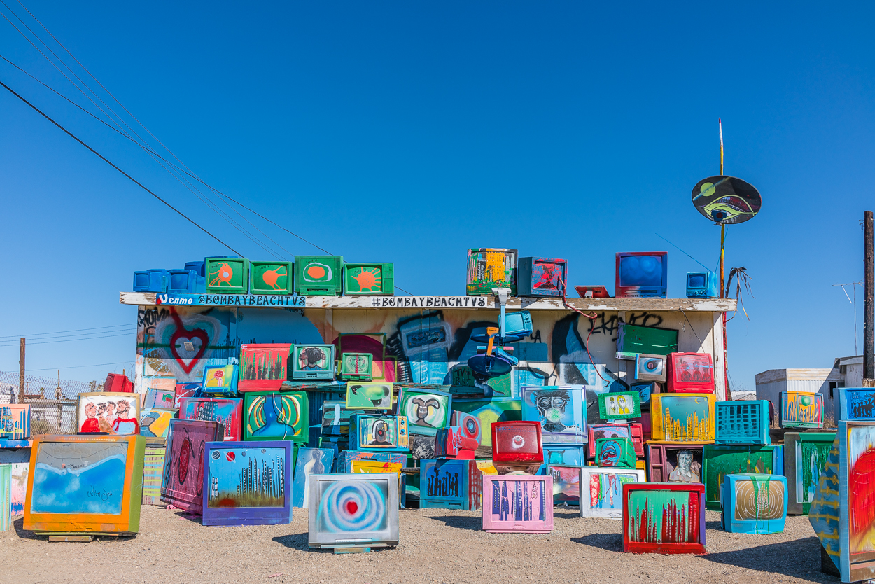 Contemporary art installation consisting of many sizes of painted television sets displayed on the ground, on the roof of a building in the settlement of Bombay Beach, California.