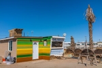 A trailer that has been added onto with a very colorful paint job and the wording {quote}The Nest{quote} with two dead palm trees beside it in the settlement of Bombay Beach, California.