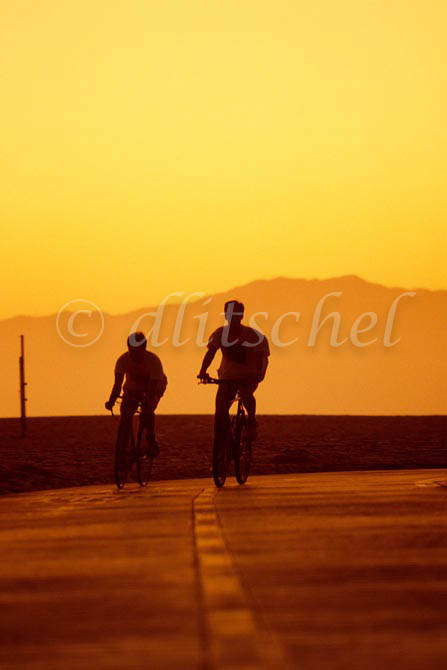 Two bicycle riders are silhouetted against mountains during a golden sunset in Santa Monica, California. To purchase this image, please go to my stock agency.