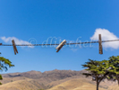 Three old weathered wooden clothes pins are attached to a clothes line against a soft focus background of Monterey Cypress trees, barren mountains, blue skies and white puffy cloud on Santa Cruz Island, part of the Channel Islands off of the coast of California. 