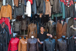 A leather salesman stares ahead as he sits down among his leather jackets and coats for sale in his stall outside the central market in Florence, Italy.