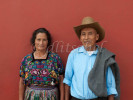 An older married couple pose against a deep terra cotta wall in their traditional dress, in Antigua, Guatemala.