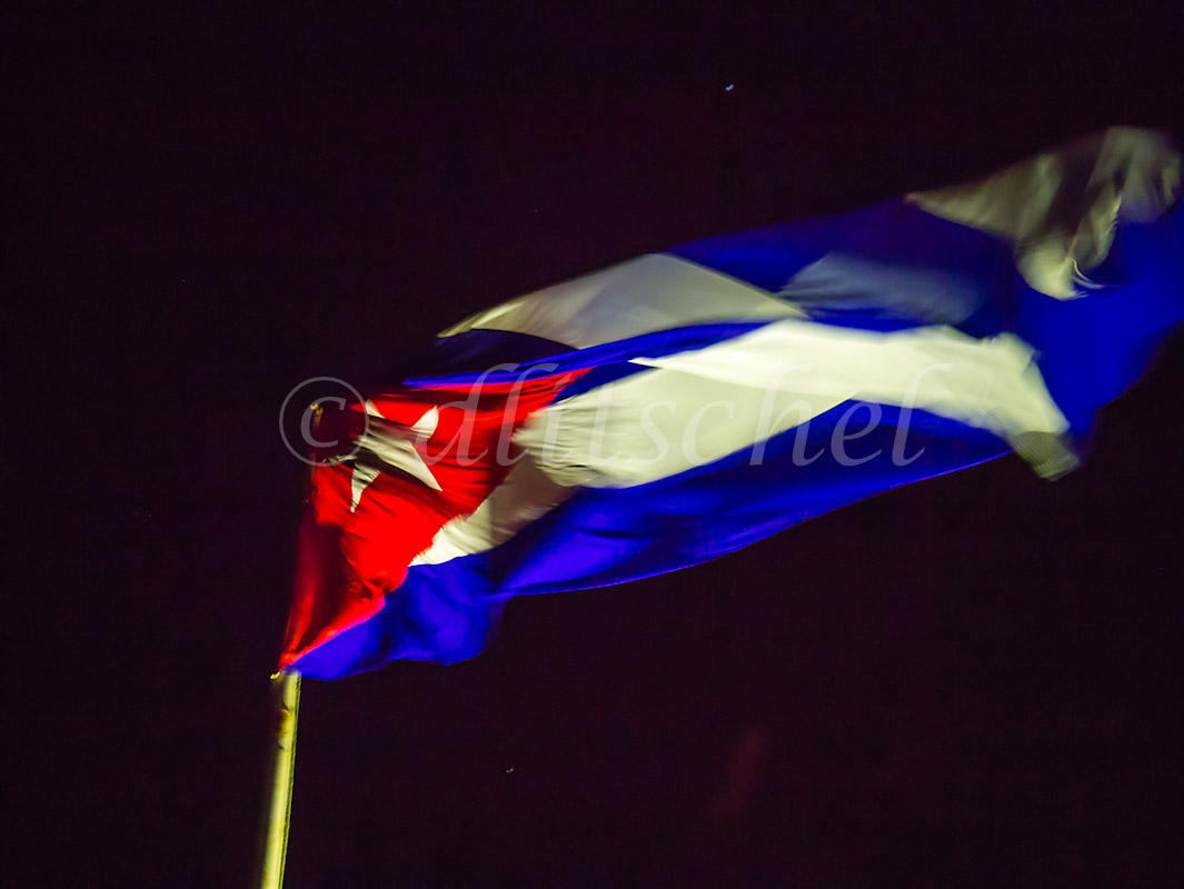 The Cuban flag flies at night lit against the black sky.