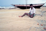 An Indiian fisherman in  Mamallapuram, India ,in the state of Tamil Nadu, sits by his boat and mends his fishing nets. To purchase this image, please go to my stock agency click here.