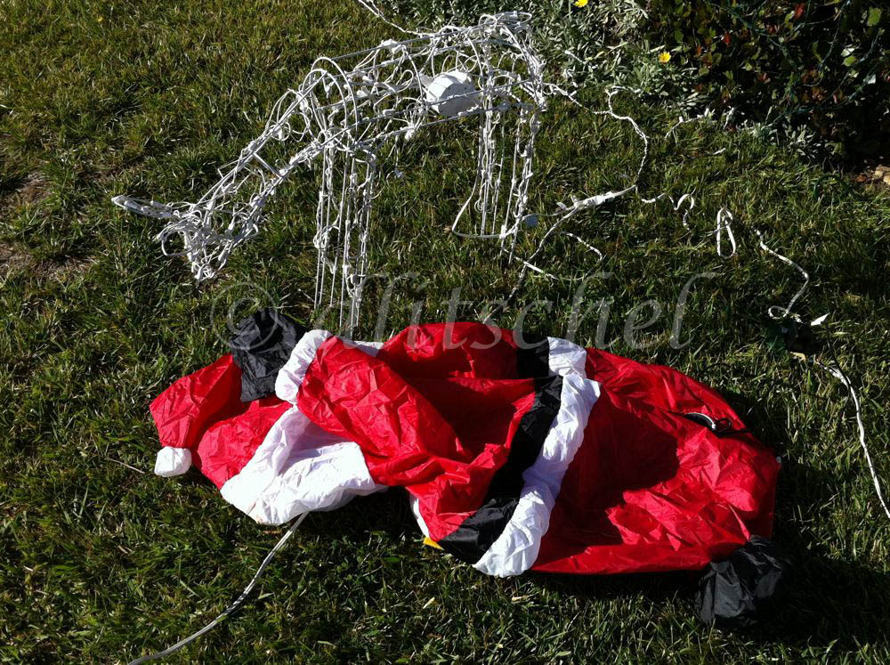 A deflated inflatable Santa Claus lies on the ground next to one of his (electronic) reindeer, aparently dead.