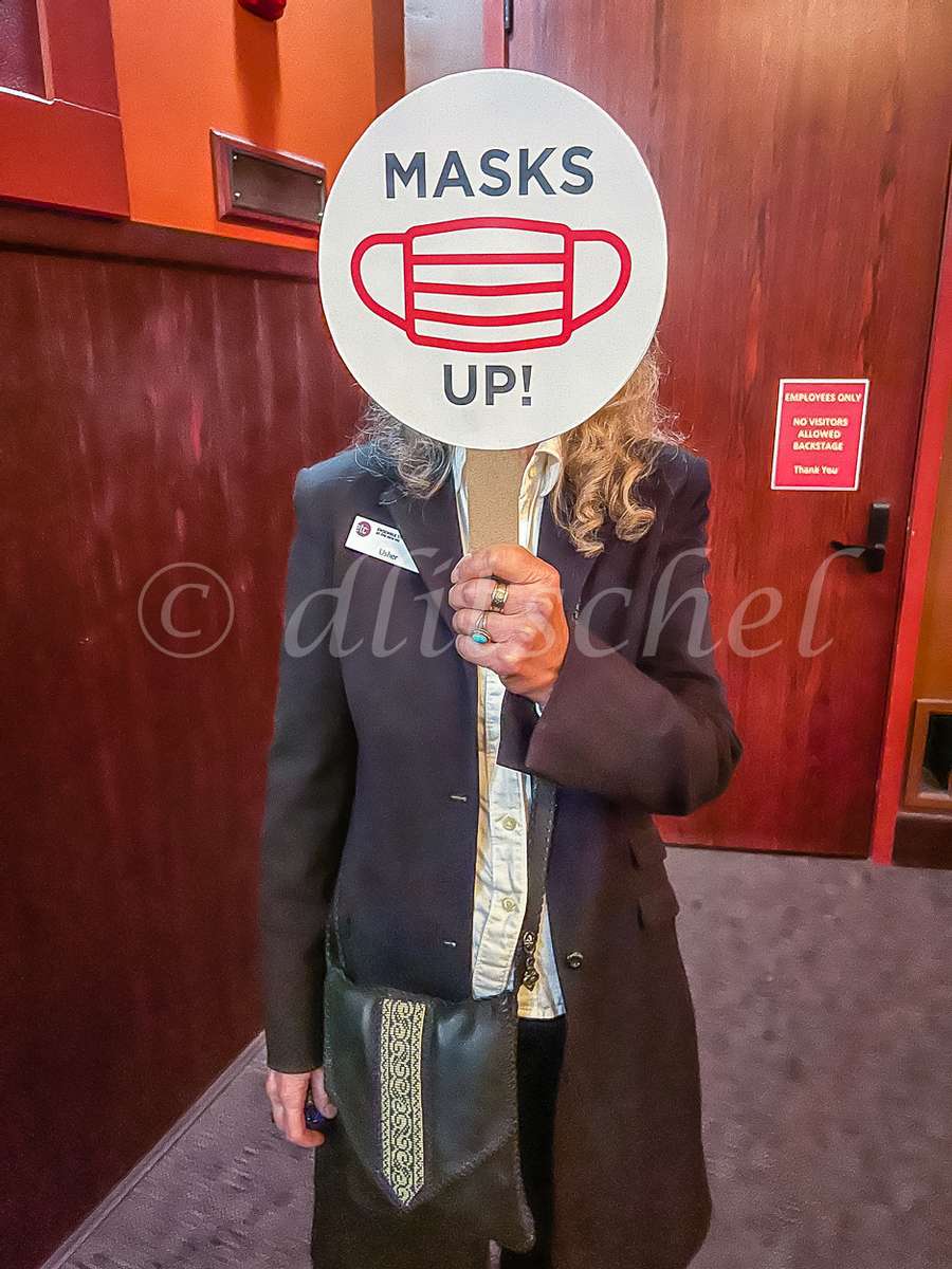 An user at the Ensemble Theater in Santa Barbara holds up a sign requiring masks to be worn at the event.