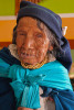 A elderly indian woman faces forward showing head and shoulders with heavily wrinkled face, poor eyesight and traditional clothing in Octovalo, Ecuador.