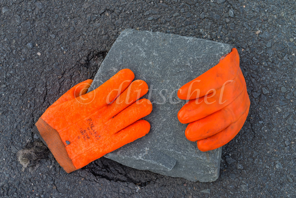 Two brilliant orange worker's gloves rest on paving stone in Peggys Cove, Nova Scotia, Canada.