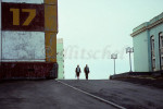 Street view Norilsk, Siberia of two pedestrians between large buildings built to with stand the pressures of the permafrost. To purchase this image, please go to my stock agency click here.