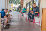 Adult males sitting, waiting for a table and focusing on their smartphones as entertainment outside a restaurant in Palm Springs, California.