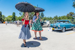 Two females in vintage clothing, walk with their parasols protecting them from the sun, at a car show in Goleta, California