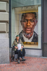 A down-and-out wheelchair bound military veteran in a green beret holds a Starbucks cup begging in front of a upscale window display in San Francisco.