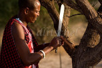 Masai warrior with machete shaping wood to use as a tool to start a fire. Sinya area of northern Tanzania. To purchase this image, please go to my stock agency click here.