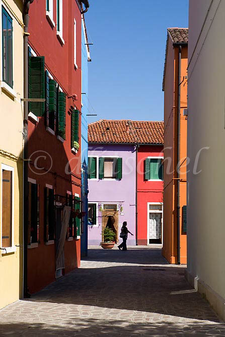 Silhouette of a woman passer by against the colorful buildings of Burano Island, Italy. To purchase this image, please go to my stock agency click here.