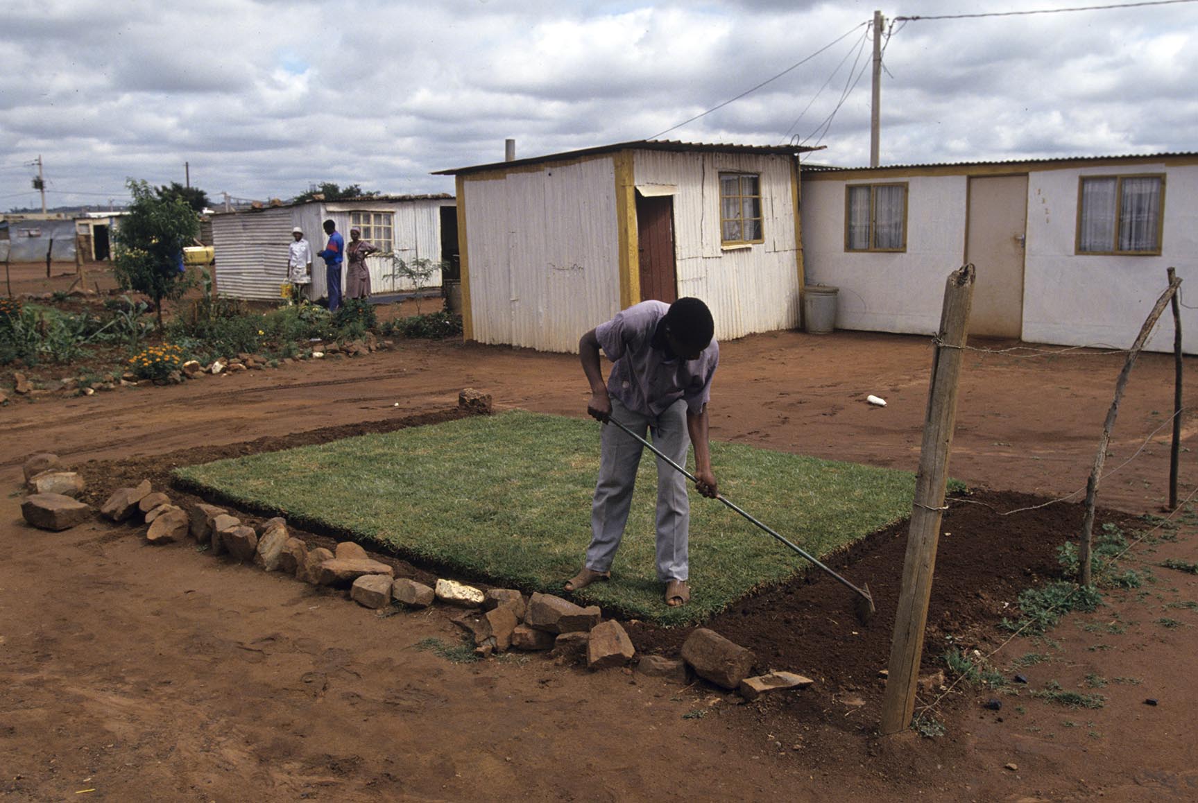 A man plants gras around shanty homes in Soweto,  an urban area of the city of Johannesburg, South Africa.  Its origins are as a very poor and impoverished black township under South Africa's Apartheid government. The population has historically been overwhelmingly black and some of the watershed events in the struggle against Apartheid occurred in the township.