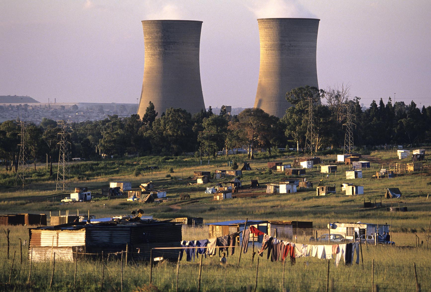 A nuclear power plant looms behind shanty homes in Soweto,  an urban area of the city of Johannesburg, South Africa.  Its origins are as a very poor and impoverished black township under South Africa's Apartheid government. The population has historically been overwhelmingly black and some of the watershed events in the struggle against Apartheid occurred in the township.