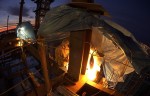 At sunrise under a blue tarp, an ironworker uses a torch to preheat a joint to 350 degrees on a 15-ton girder before welding. A small crew of welders took turns working 12-hour shifts for over 100 continuous hours to complete the job of welding the joints on two transfer girders.  Each girder came in two pieces, weighing 15 and 19.5 tons, which were erected on south side of the 55th floor of the Comcast Center. The joints on the two girders needed to remain at 350 degrees and kept dry through the duration of the welding.  