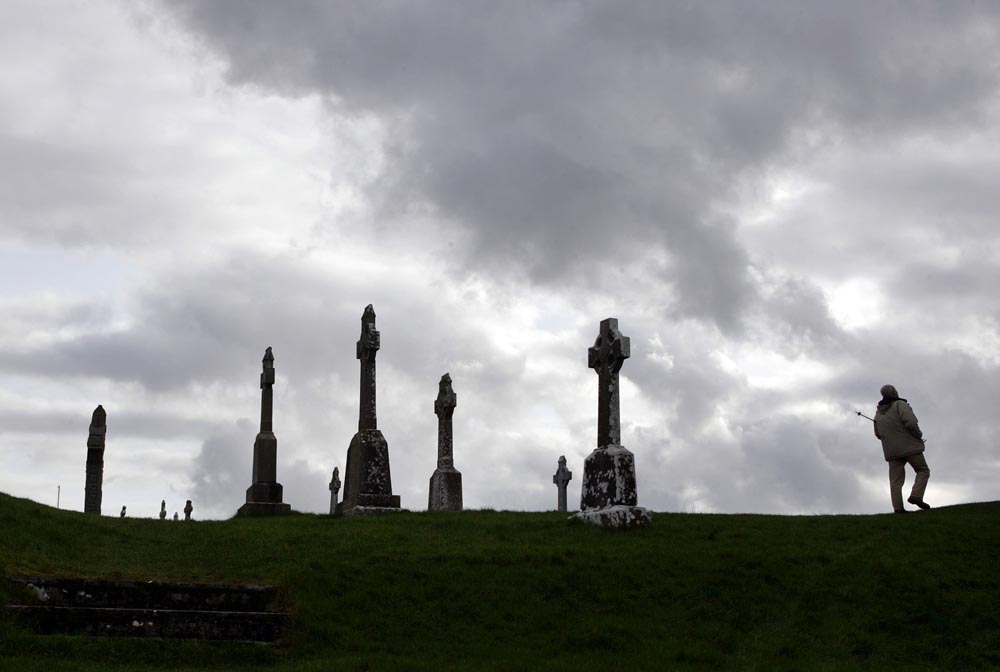 A man strolls through the ancient monastic site of Clonmacnoise overlooking the River Shannon in County Offaly of Ireland. The site was founded by St. Ciaran in 548 AD and includes numerous early churches, high crosses, two round towers and a large collection of early Christian grave slabs. 