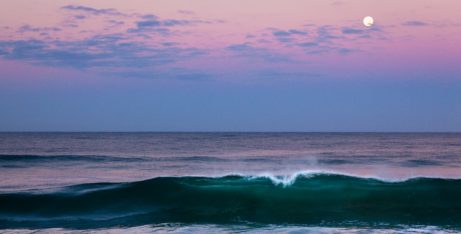 A full moon above a wave just before sunrise on the beach in front of Rancho Pescadero near Todos Santos, Baja.