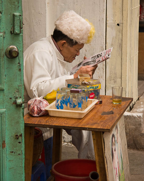 Street merchant reading the news paper. Photo by Jay Graham